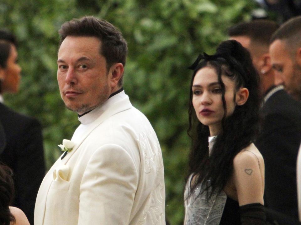 Elon Musk stands next to Grimes outdoors