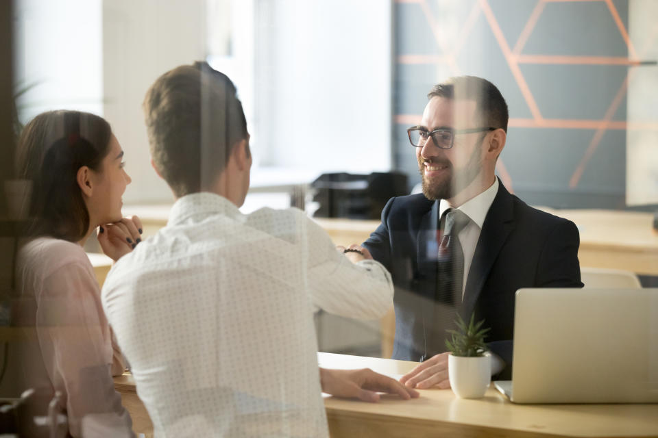 A banker reaches across his desk to shake hands with customers.