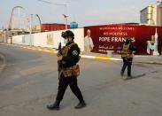 Iraqi security members walk near a poster of Pope Francis ahead of his arrival, in Baghdad