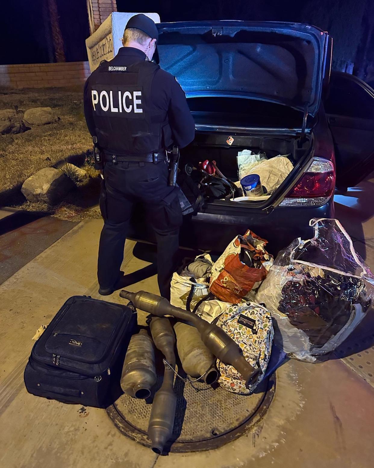 A police officer searches the Toyota Camry that led police on a chase through south Palm Springs that injured two officers on Tuesday. Stolen catalytic converters that were seized from the vehicle are visible behind the officer.