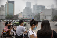 People wearing face masks to protect against the coronavirus wait to cross an intersection in Beijing, Saturday, July 11, 2020. New coronavirus cases have dropped sharply in China, and authorities are turning their attention to concerns that the virus could spread through imported food. (AP Photo/Mark Schiefelbein)