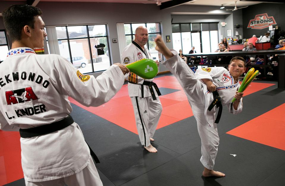 Fifth degree Black Belt and instructor owner Michael Poole (middle in background) watches as Jaxon Lowry, 10 of Lancaster, practices his kicks as Liam Kinder, 16 of Carroll, holds a target for him to kick inside of the Lancaster ATA Martial Arts on July 31, 2023, in Lancaster, Ohio. The Taekwondo students, along with instructor Michael Poole, went to the ATA World Championships in Phoenix, Arizona where Kinder took third in traditional sparring, and Evelyn Hill (not shown), 16, took first place in extreme weapons. Lowry did not place in worlds but won first place in traditional sparring and combat at the state level championship.