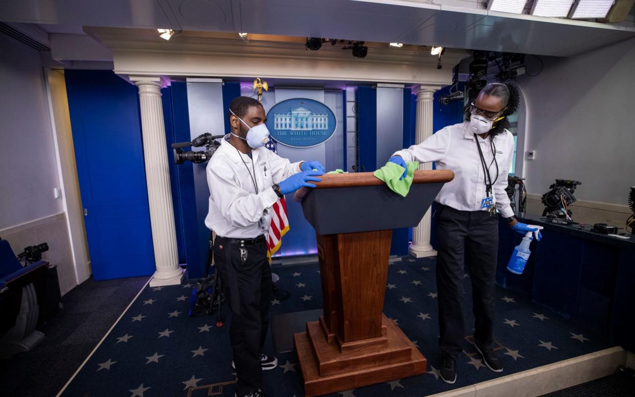 A cleaning crew wipes down the White House press briefing room's lectern in April 2020 - Alex Brandon /AP