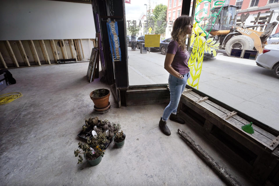 Jenny Sebold, owner of Rebel Heart clothing and gift store and Pink Shutter Flowers, stands next to dead flowers as a loader passes her destroyed business, Tuesday, Aug. 1, 2023, in Montpelier, Vt. The mostly gutted shops, restaurants and businesses that lend downtown Montpelier its charm are considering where and how to rebuild in an era when extreme weather is occurring more often. Vermont's flooding was just one of several major flood events around the globe this summer that scientists have said are becoming more likely due to climate change. (AP Photo/Charles Krupa)