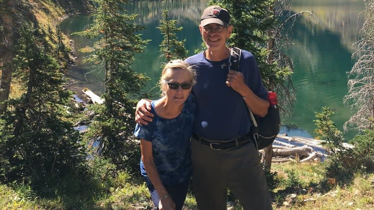 Dana Holby and Rich Moore embrace by a mountain lake. 