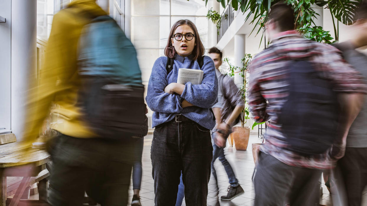 Fearful female student looking at camera while other students are walking around her in blurred motion.