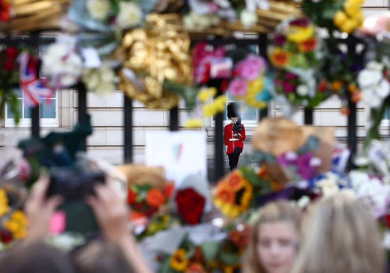 Un guardia es visto mientras la gente ve y coloca ofrendas florales en las puertas del Palacio de Buckingham, tras la muerte de la reina Isabel II, en Londres, Reino Unido