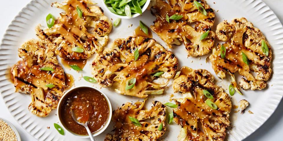 grilled teriyaki cauliflower steaks on a platter with more teriyaki sauce and scallions