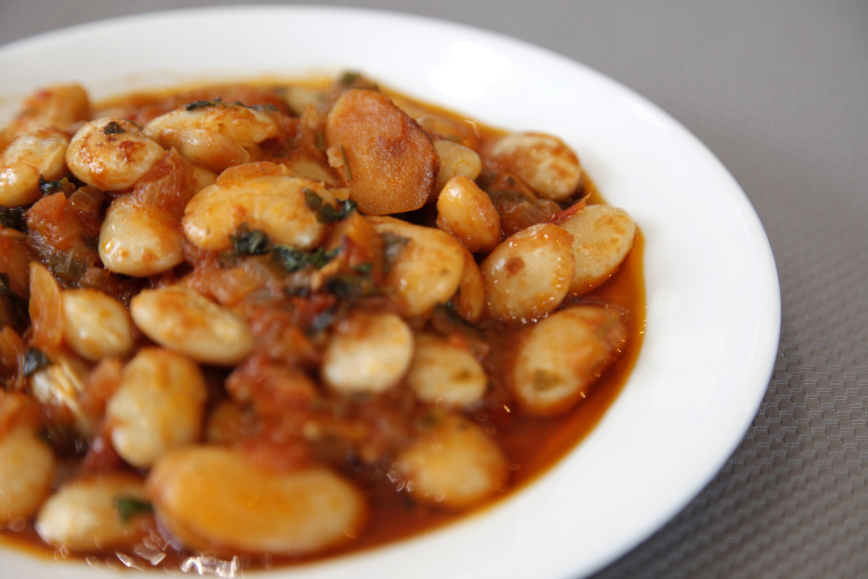 Closeup of Greek baked beans, Gigantes Plaki, in a white porcelain bowl, selective focus, blurred around the edges