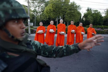 A Thai soldier stands guard while Buddhist monks beg for alms outside a temple near Government House in Bangkok in this May 23, 2014 file photograph. REUTERS/Athit Perawongmetha/Files