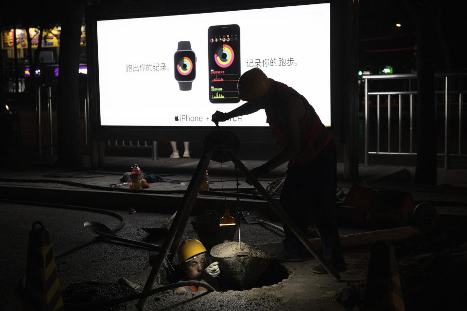 A worker hauls earth from a hole in the ground near advertisement for tech products in Beijing on Tuesday, July 14, 2020. China's economy rebounded from a painful contraction to grow by 3.2% over a year earlier in the latest quarter as anti-virus lockdowns were lifted and factories and stores reopened. (AP Photo/Ng Han Guan)