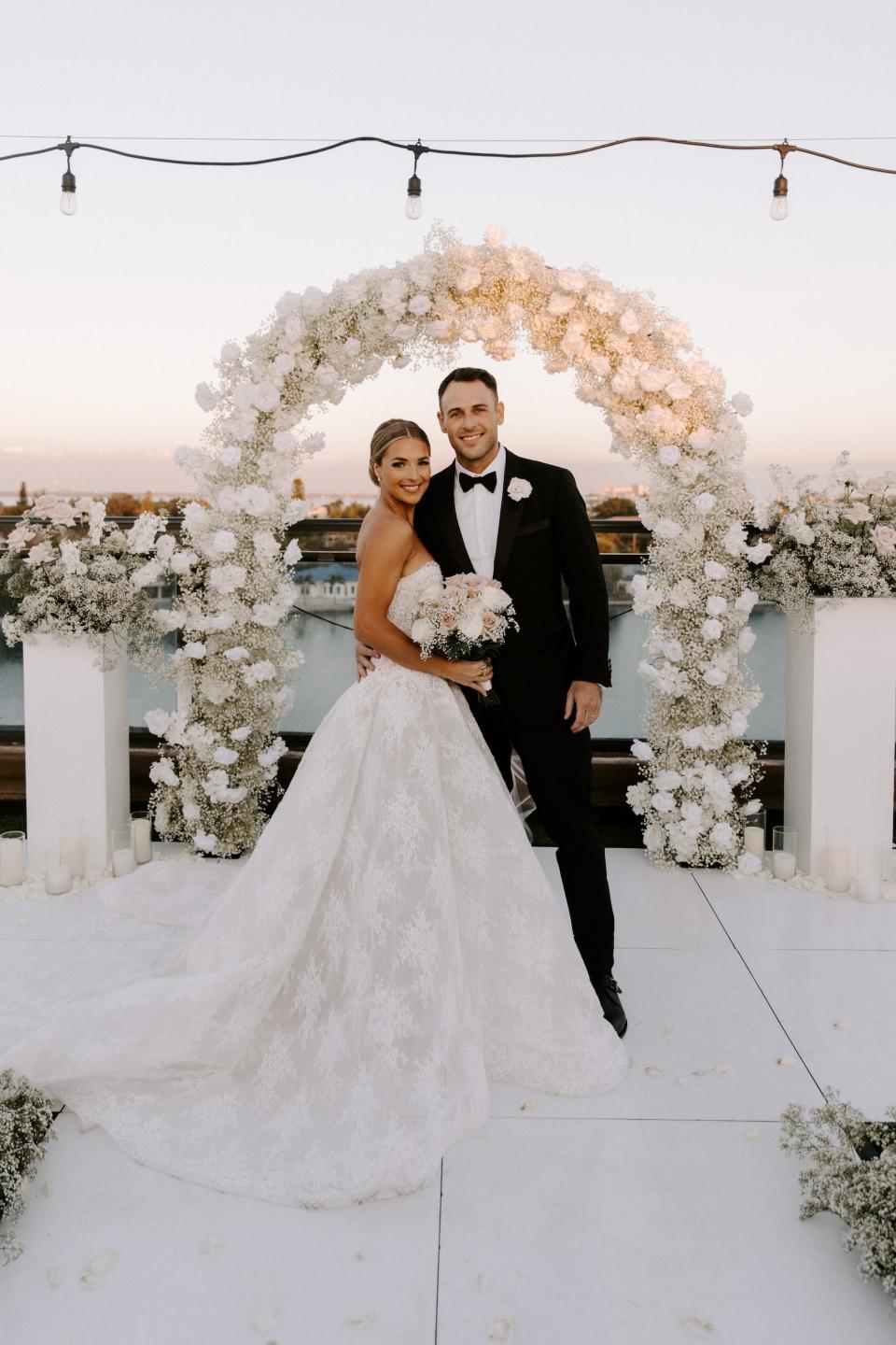 A bride and groom embrace in front of a floral arch.