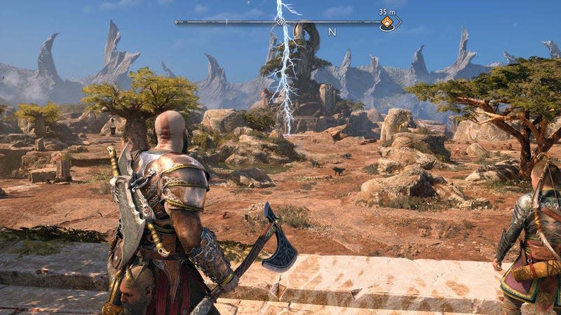 Kratos stands on top of a small hill and looks out at a large, desert-like area. 