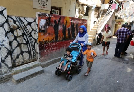 A woman pushes a baby cart as she walks past graffiti at Shatila refugee camp in Beirut
