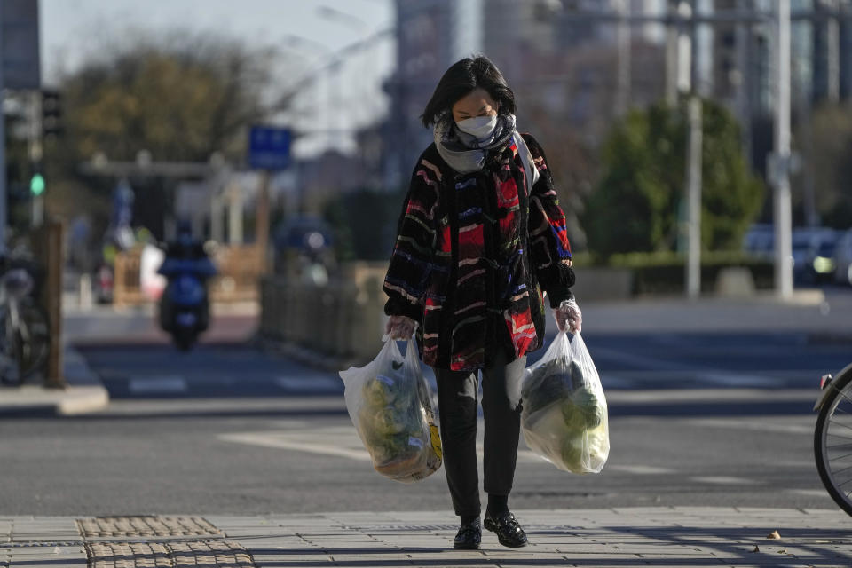 A woman wearing a face mask and groves carries bags of groceries walks on a street in Beijing, Monday, Dec. 5, 2022. China is easing some of the world's most stringent anti-virus controls and authorities say new variants are weaker. But they have yet to say when they might end a "zero-COVID" strategy that confines millions of people to their homes and set off protests and demands for President Xi Jinping to resign. (AP Photo/Andy Wong)