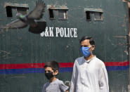 A Kashmiri man and a child wearing masks walk past a parked armored police vehicle in Srinagar, Indian controlled Kashmir, Monday, July 13, 2020. Authorities reimposed lockdown on Monday in parts of Indian-controlled Kashmir, including the region's main city, following surge in coronavirus cases. (AP Photo/Mukhtar Khan)