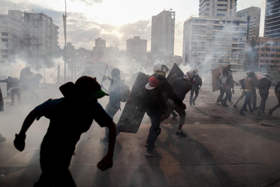 Demonstrators take cover from teargas fired by the police during clashes in an anti-government protest in Caracas, Venezuela, Monday, March 10, 2014. The Venezuelan government and opposition appear to have reached a stalemate, in which street protests continue almost daily while the opposition sits out a peace process it calls farcical. (AP Photo/Alejandro Cegarra)