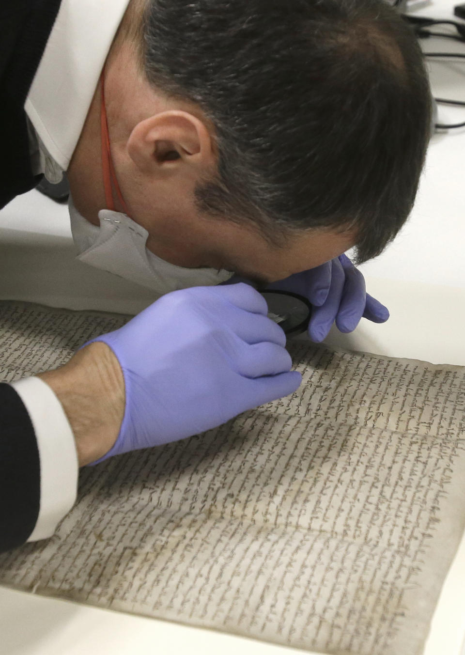 In this Wednesday, Feb. 5, 2014 photo, wearing special gloves and a mask, Chris Woods, director of London's National Conservation Service, uses a magnifying glass to inspect the Magna Carta, after its arrival in Houston. The centuries old parchment, which has never left England before, will be on display at the Houston Museum of Natural Science for six months starting Feb. 14, 2014. (AP Photo/Pat Sullivan)