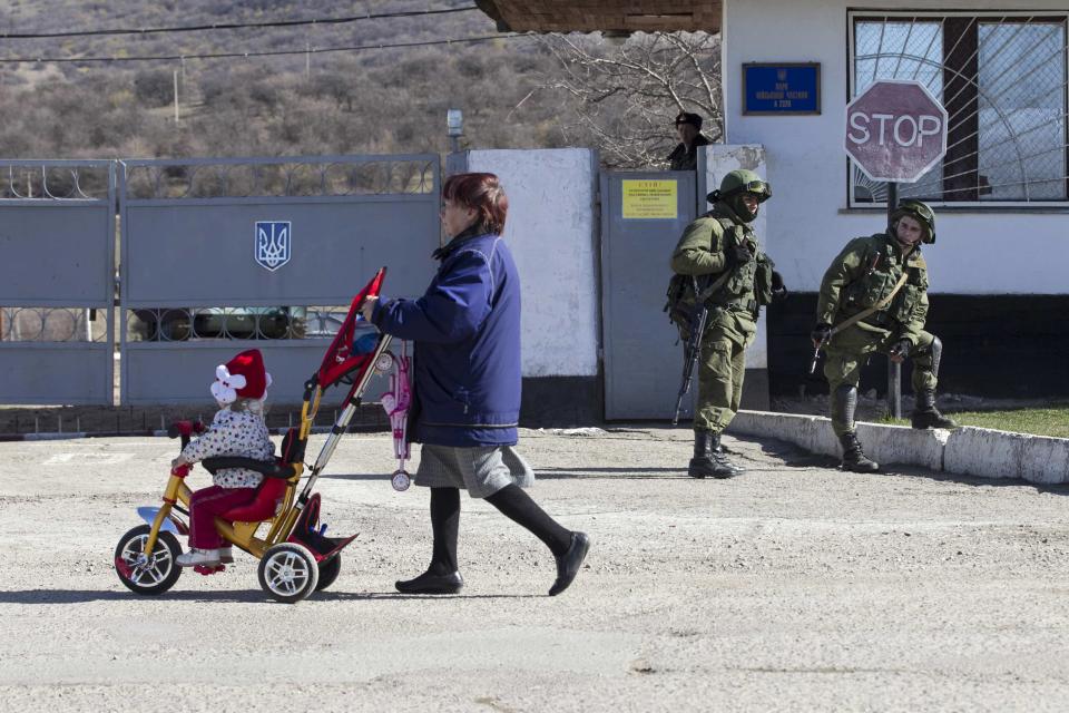 A Ukrainian woman walks past military personnel, believed to be Russian servicemen, outside the territory of a Ukrainian military unit in the village of Perevalnoye