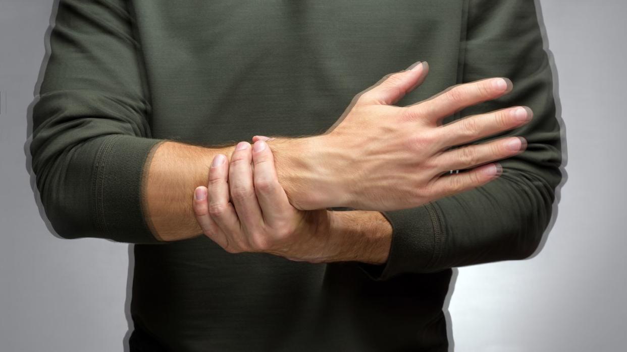 a man with a tremor tries to keep his hand from trembling with t