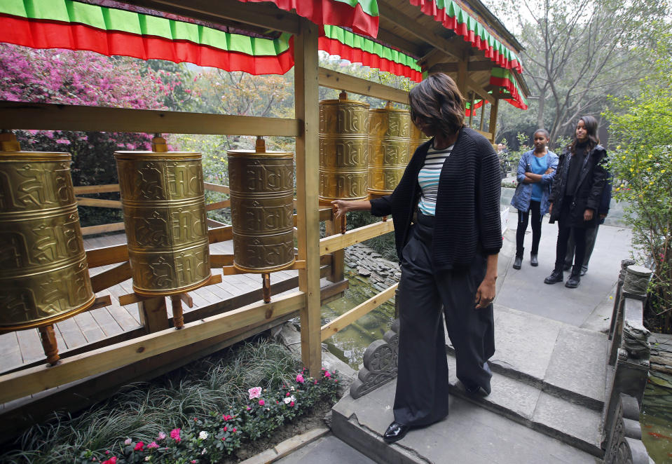 U.S. first lady Michelle Obama, left, touches Tibetan prayer wheels as her daughter Malia, right, and Sasha watch outside a Tibetan restaurant in Chengdu, Sichuan province, China Wednesday, March 26, 2014. (AP Photo/Petar Kujundzic, Pool)