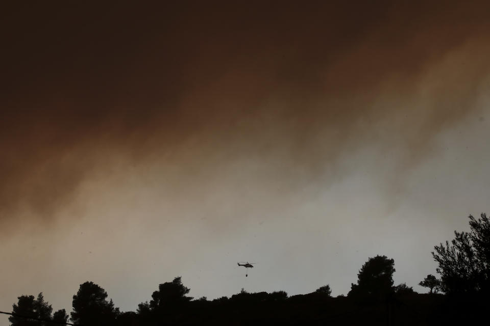 A firefighting helicopter flies below a thick cloud of smoke from a forest fire at Psachna village on the island of Evia, northeast of Athens, Tuesday, Aug. 13, 2019. Dozens of firefighters backed by water-dropping aircraft are battling a wildfire on the island that has left the Greek capital blanketed in smoke. (AP Photo/Yorgos Karahalis)