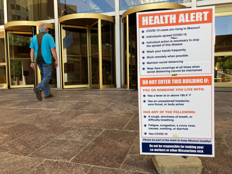 FILE - In this June 15, 2021 file photo, a sign warning of COVID-19 dangers remains in place outside the entryway of a state office building in Jefferson City, Mo. Companies around the U.S. are scrambling to figure out how to bring employees back to the office after more than a year of them working remotely. Most are proceeding cautiously, trying to navigate declining COVID-19 infections against a potential backlash by workers who are not ready to return. (AP Photo/David A. Lieb)