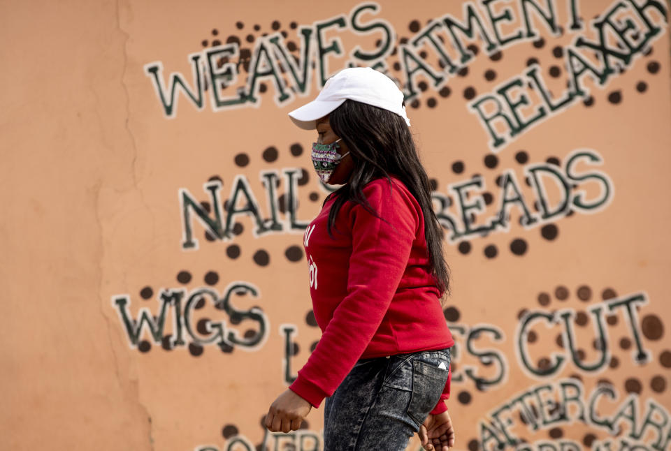 A woman wearing a face mask to protect herself against coronavirus, walks past a closed hair salon at Tembisa township in Johannesburg, South Africa, Tuesday, May 19, 2020. (AP Photo/Themba Hadebe)