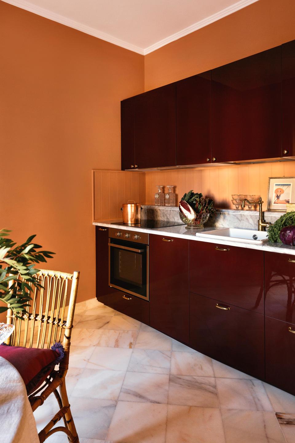 Mirta shifted the kitchen to achieve an open-plan layout and opted for a contrasting look of glossy burgundy millwork and terra-cotta-colored walls. She also added wooden paneling, a Carrara marble top, and brass details, although according to her, it’s the framed vintage Vogue covers occupying the shelf that are the real stars. “They’re what served as the lodestar for the renovation,” she muses. The cushion on the chair is from Mirta’s homeware collection. A tablecloth from Zara Home acts as a calming antidote to the surrounding color.