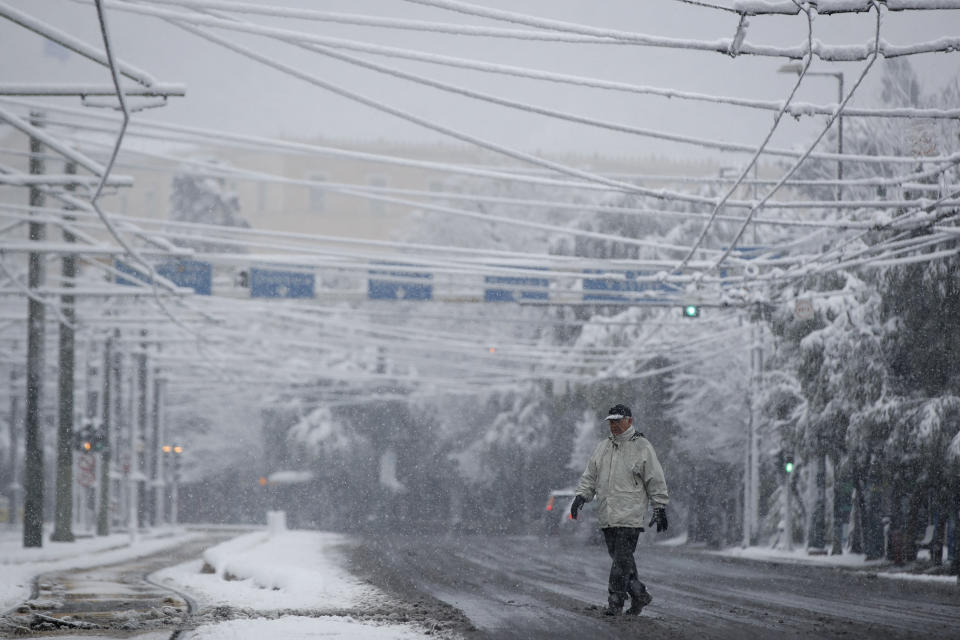 A man walks during a heavy snowfall in central Athens, Tuesday, Feb.16, 2021. Unusually heavy snowfall has blanketed central Athens, with authorities warning residents particularly in the Greek capital's northern and eastern suburbs to avoid leaving their homes. (AP Photo/Thanassis Stavrakis)
