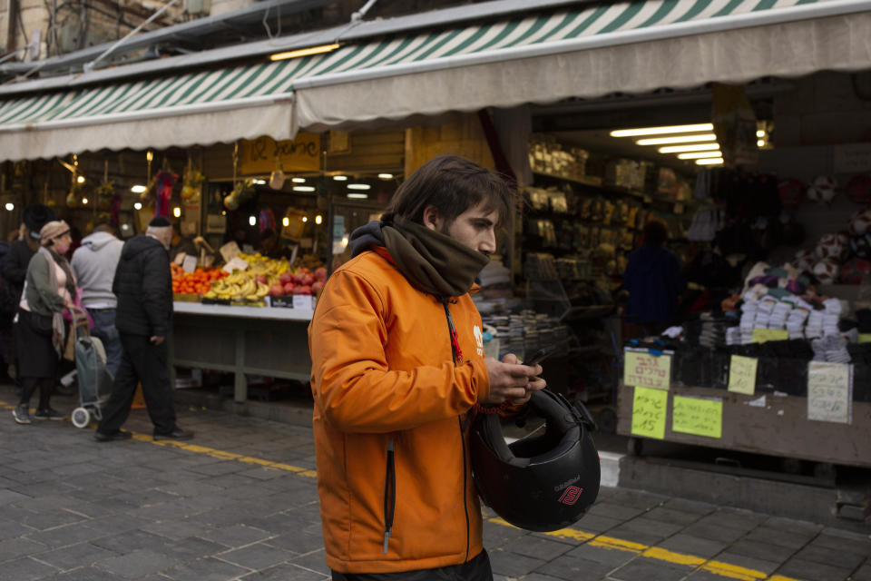 A dood delivery driver carries his smart phone in the Mahane Yehuda market in Jerusalem, Wednesday, Dec. 23, 2020. In the early days of the pandemic, a panicked Israel began using a mass surveillance tool on its own people, tracking civilians’ mobile phones to halt the spread of the coronavirus. But months later, the tool’s effectiveness is being called into question and critics say its use has come at an immeasurable cost to the country’s democratic principles. (AP Photo/Maya Alleruzzo)