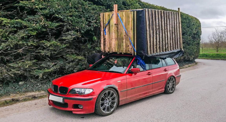 A red BMW with a shed strapped to its roof from a front-on angle.