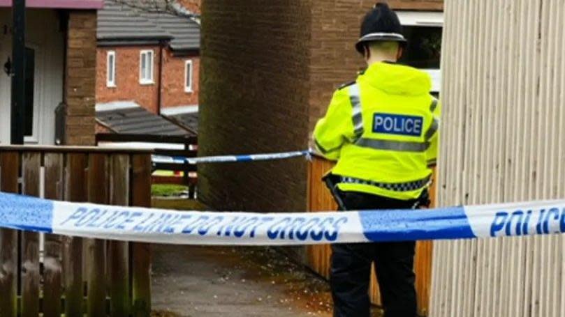 A police officer outside a house, behind police tape