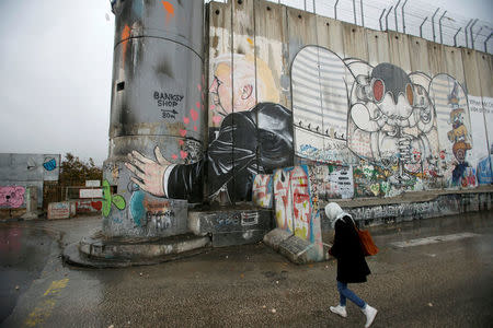 A Palestinian woman walks next to a mural depicting U.S. President Donald Trump that is painted on a part of the Israeli barrier, in the West Bank city of Bethlehem December 6, 2017. REUTERS/Mussa Qawasma
