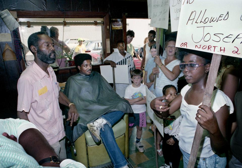 Metro Councilman Vernon Winfrey, left, cuts a customer's hair as his Bayard Avenue barbershop while listening to a constituent's community concerns on Aug. 3, 1990.