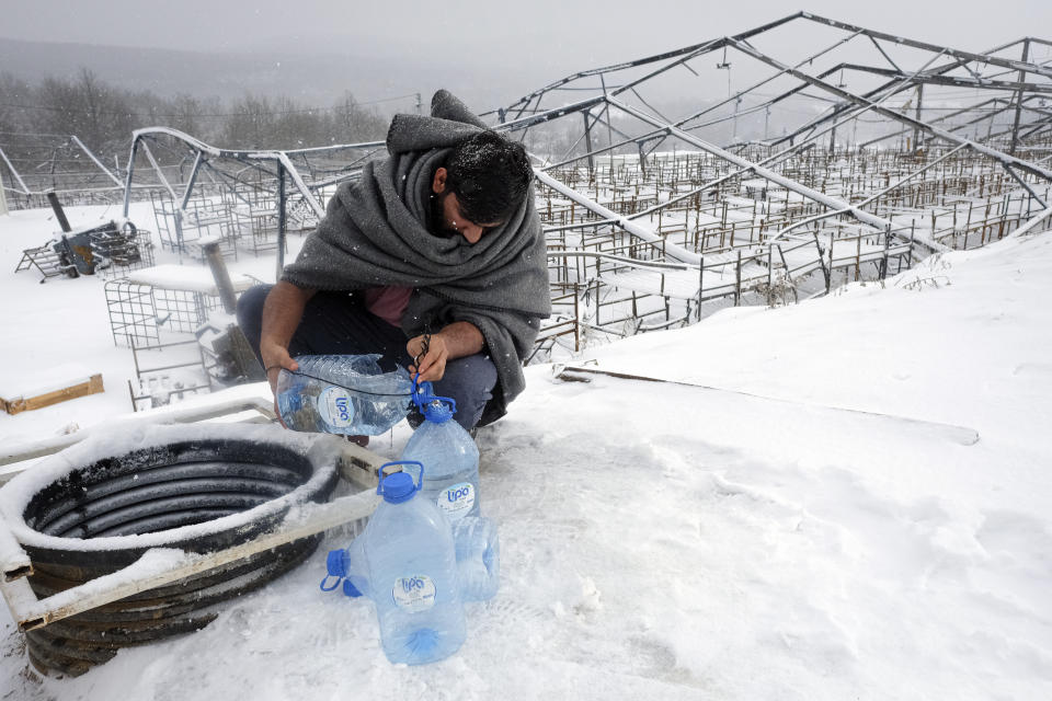 A migrant uses plastic bottles to take water out of a well during a snowfall at the Lipa camp, outside Bihac, Bosnia, Monday, Jan. 11, 2021. Aid workers say migrants staying at a camp in northwestern Bosnia have complained or respiratory and skin diseases after spending days in make-shift tents and containers amid freezing weather and snow blizzards. Most of the hundreds of migrants at the Lipa facility near Bosnia's border with Croatia on Monday have been accommodated in heated military tents following days of uncertainty after a fire gutted most of the camp on Dec. 23. (AP Photo/Kemal Softic)