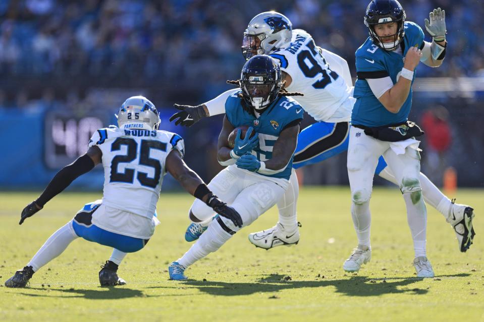 Jacksonville Jaguars running back D'Ernest Johnson (25) rushes for yards as Carolina Panthers safety Xavier Woods (25) looks to tackle as Panthers linebacker Yetur Gross-Matos (97), back, can’t make a tackle and Jaguars quarterback C.J. Beathard (3) looks on during the third quarter of a regular season NFL football matchup Sunday, Dec. 31, 2023 at EverBank Stadium in Jacksonville, Fla. The Jacksonville Jaguars blanked the Carolina Panthers 26-0. [Corey Perrine/Florida Times-Union]