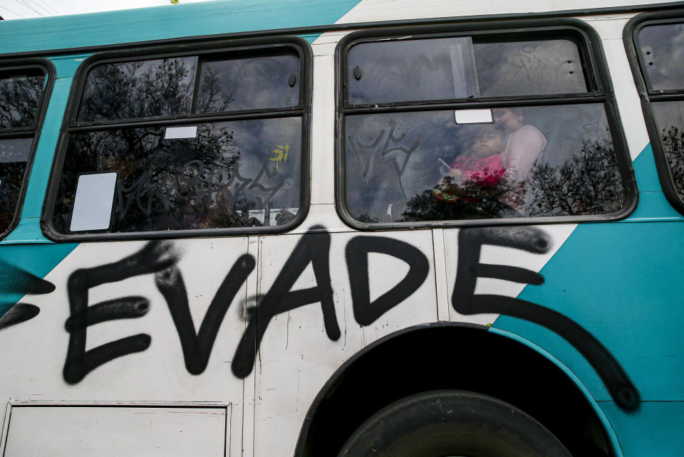 People travel in a bus painted with graffiti that reads in Spanish "Evade," in Santiago, Chile, Saturday, Oct. 19, 2019. Chile has been facing protests that started on Friday afternoon when high school students flooded subway stations, jumping turnstiles, dodging fares and vandalizing stations as part of protests against a fare hike, but by nightfall had extended throughout Santiago with students setting up barricades and fires at the entrances to subway stations, forcing President Sebastian Pinera to announce a state of emergency and deploy the armed forces into the streets. (AP Photo/Esteban Felix)