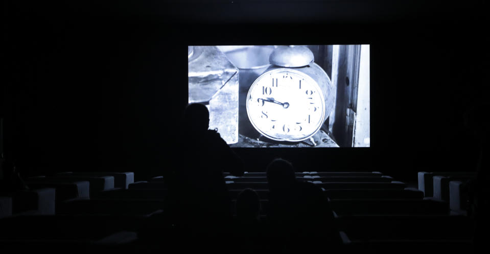 People watch a section of the 24 hour video installation by Christian Marclay entitled ' The Clock' at the Tate Modern in London, Tuesday, Sept. 11, 2018. Christian Marclay's "The Clock" is both the ultimate movie, and an artwork you can set your watch by. The Swiss-American artist has edited together thousands of film clips containing clocks, watches or references to the time _ one or more for every minute of the day _ into a 24-hour video. It’s a mesmerizing patchwork that moves forward in time as it dances back and forth across film history. (AP Photo/Alastair Grant)