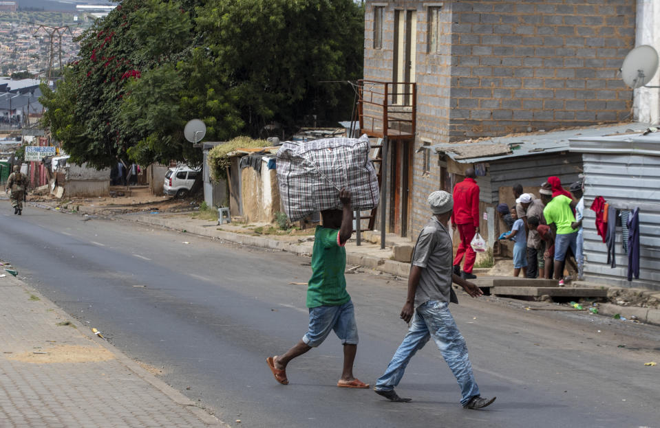 A man carrying a bag on his had crosses the street as the South African National Defence Forces patrol a densely populated Alexandra township east of Johannesburg, South Africa, Saturday, March 28, 2020. South Africa went into a nationwide lockdown for 21 days in an effort to control the spread of the COVID-19 coronavirus. The new coronavirus causes mild or moderate symptoms for most people, but for some, especially older adults and people with existing health problems, it can cause more severe illness or death. (AP Photo/Themba Hadebe)