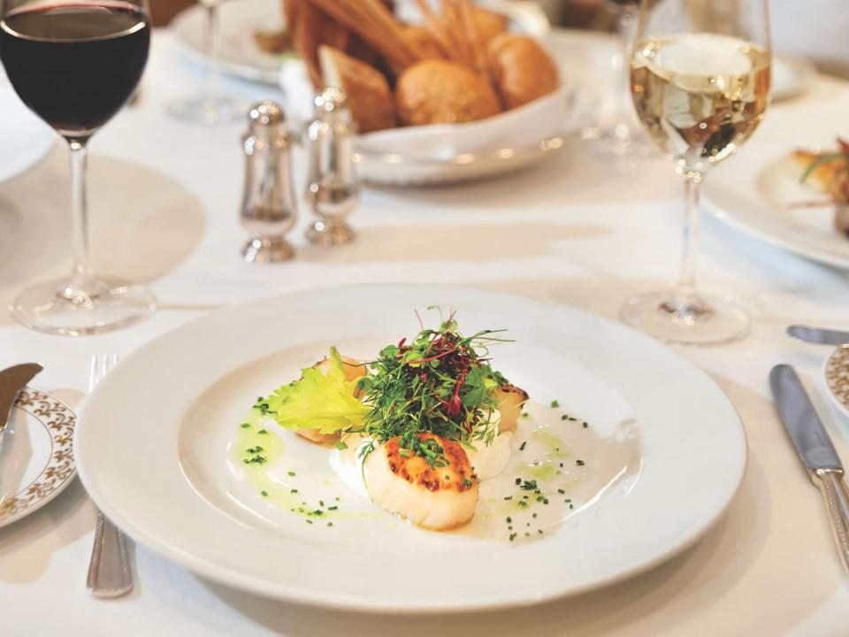 A chef serving food on a table. There's a plate of food in the front of the frame.