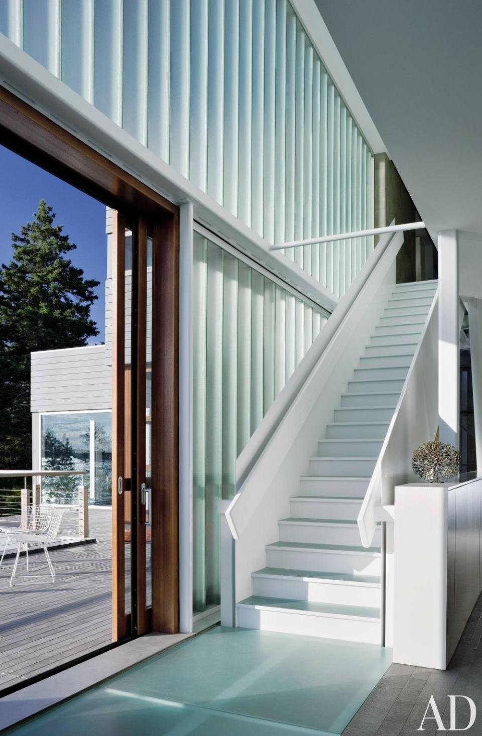 A sliding door opens onto the afternoon porch on the main level of a <a rel="nofollow noopener" href="https://www.architecturaldigest.com/story/beyond-the-box-article?mbid=synd_yahoo_rss" target="_blank" data-ylk="slk:house on Maine's Penobscot Bay;elm:context_link;itc:0;sec:content-canvas" class="link ">house on Maine's Penobscot Bay</a>. The painted-steel stair, with glass treads, leads to the top floor.