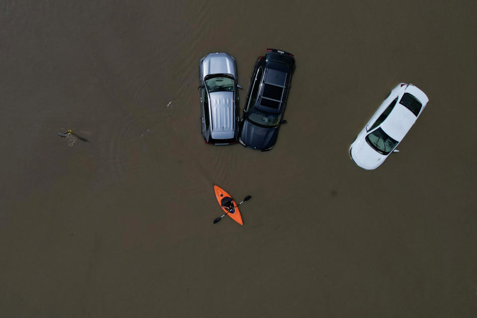 A person in a canoe passes three cars partially submerged by floodwaters. 