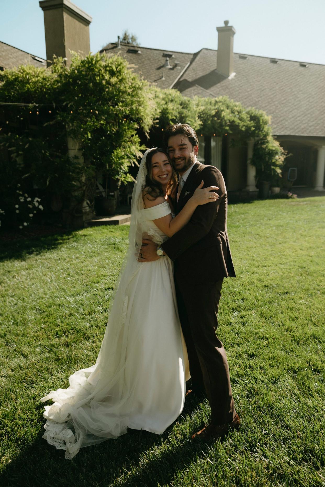 A bride and groom embracing in a grassy field.