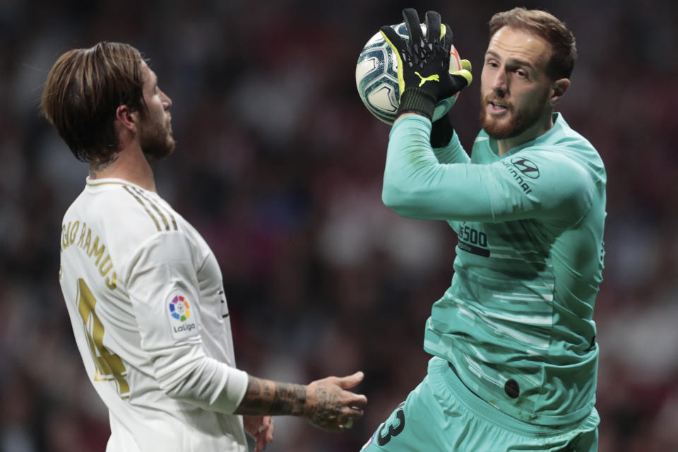 El arquero Jan Oblak del Atlético de Madrid con el balón ante el defensor Sergio Ramos del Real Madrid, en el estadio Wanda Metropolitano en Madrid, el sábado 28 de septiembre de 2019. (AP Foto/Bernat Armangue)