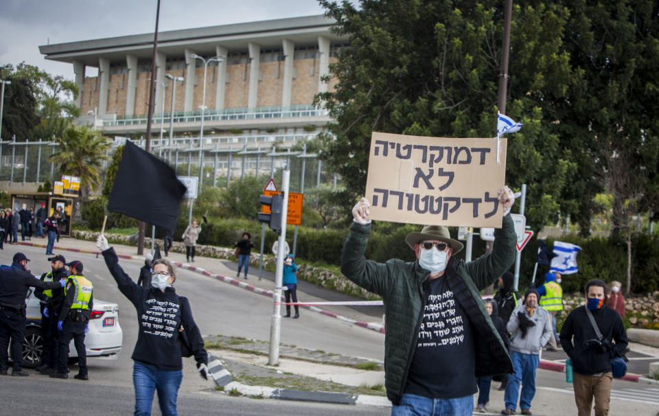 A man holds a sign that reads in Hebrew; "Democracy, No to Dictatorship" during a protest outside the Israeli parliament in Jerusalem, Thursday, March 19, 2020. Hundreds of people defied restrictions on large gatherings to protest outside parliament Thursday, while scores of others were blocked by police from reaching the area as they accused Prime Minister Benjamin Netanyahu's government of exploiting the coronavirus crisis to solidify his power and undermine Israel's democratic foundations. (AP Photo/Eyal Warshavsky)