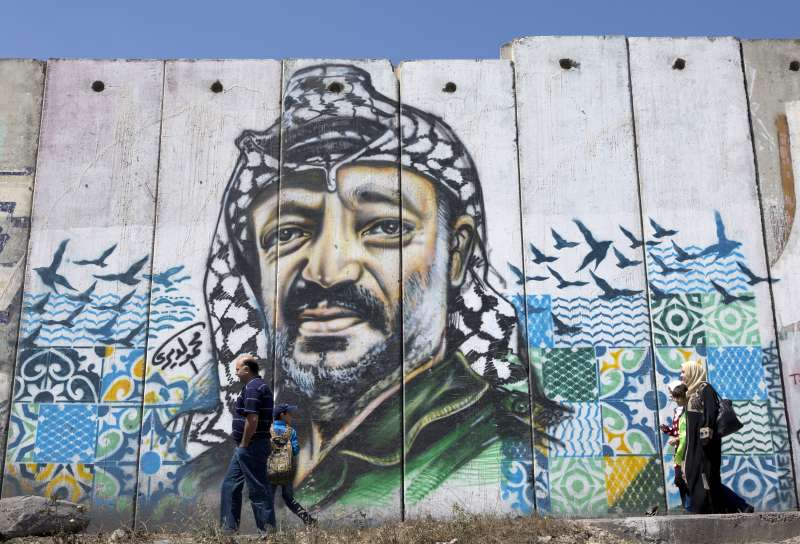 巴勒斯坦民眾走過以色列興建的「隔離牆」，上頭還畫著巴勒斯坦前領導人阿拉法特的肖像。