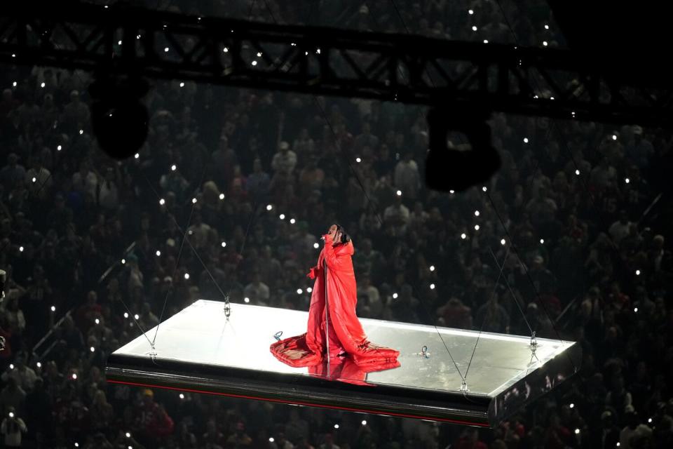 A woman in a red outfit stands on a white platform and sings.