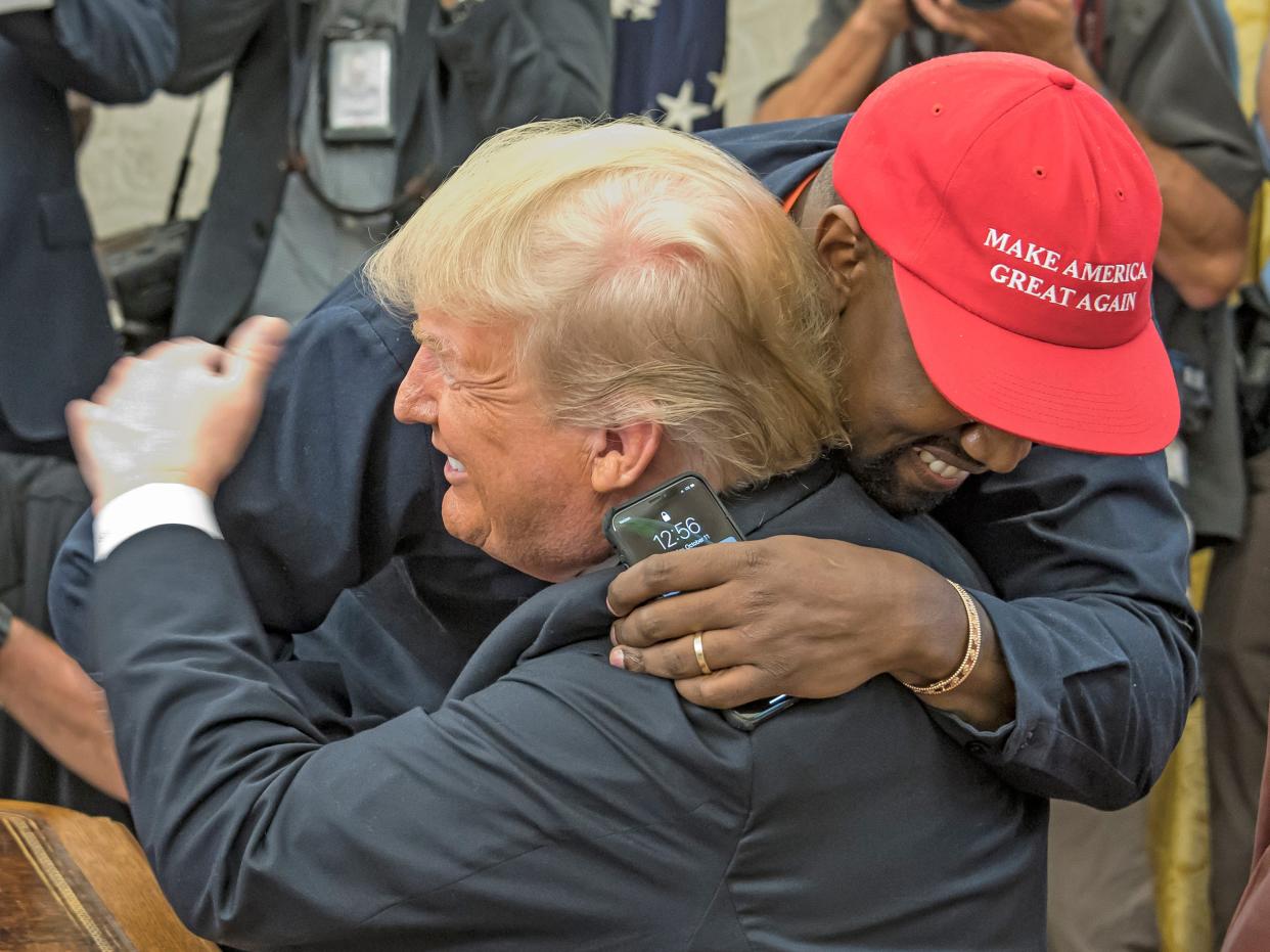 Kanye West, in a red MAGA hat, hugs DOnald Trump in the Oval Office.