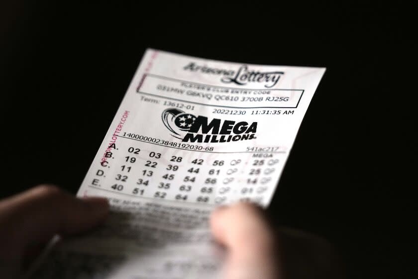 A very close-up view of a hand holding a Mega Millions lottery ticket against a black backdrop.